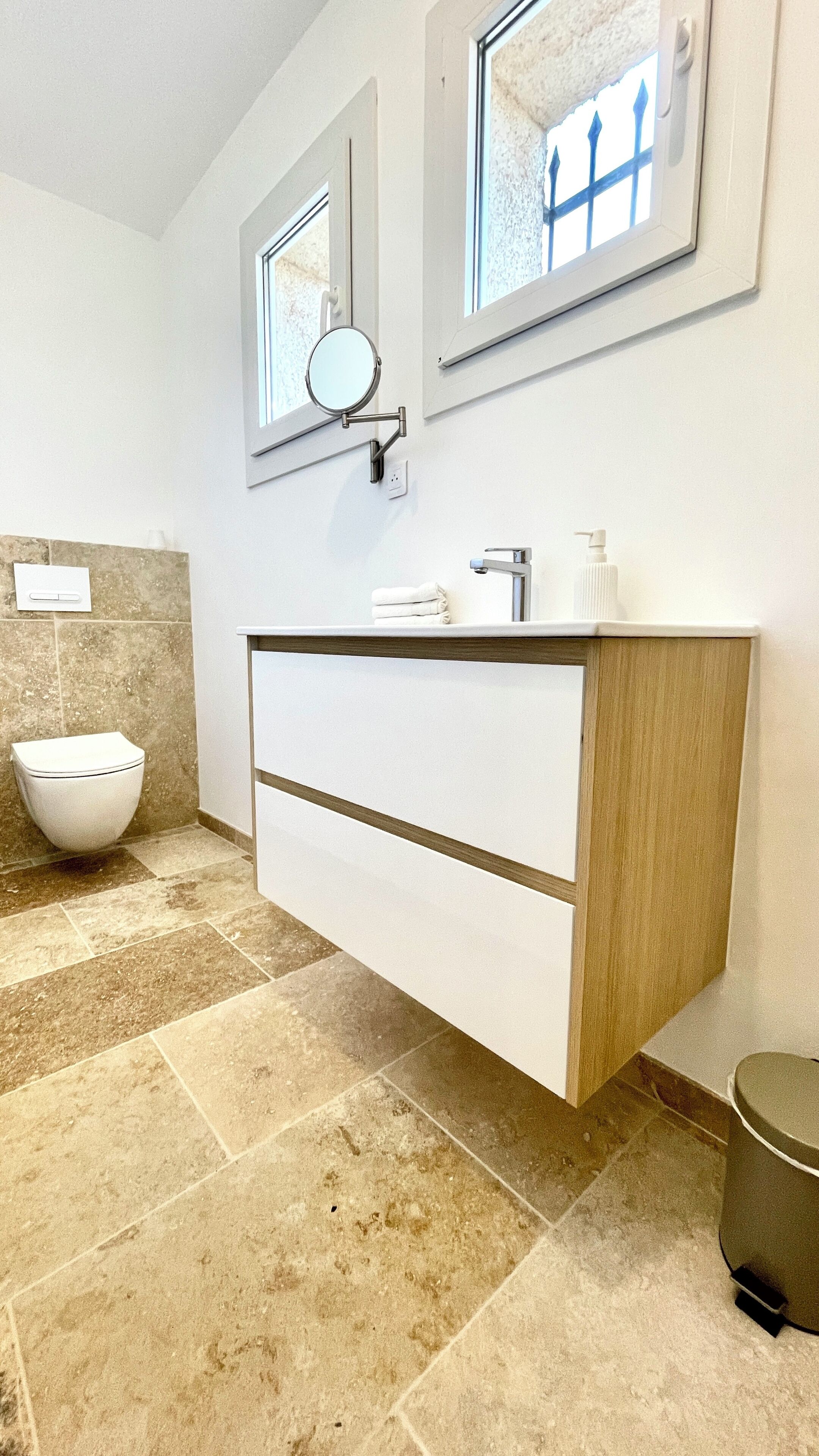 Un bany modern amb un lavabo blanc, un mirall rodó i un vàter.