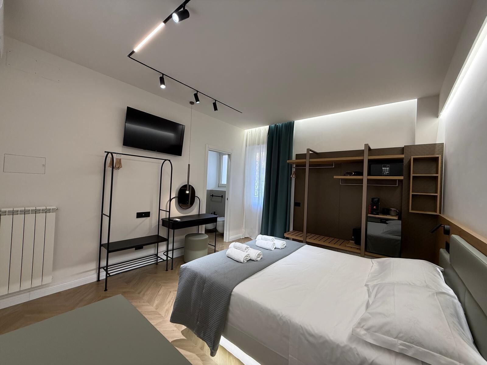 A modern hotel room with a bed, a desk, a TV, and a walk-in closet.