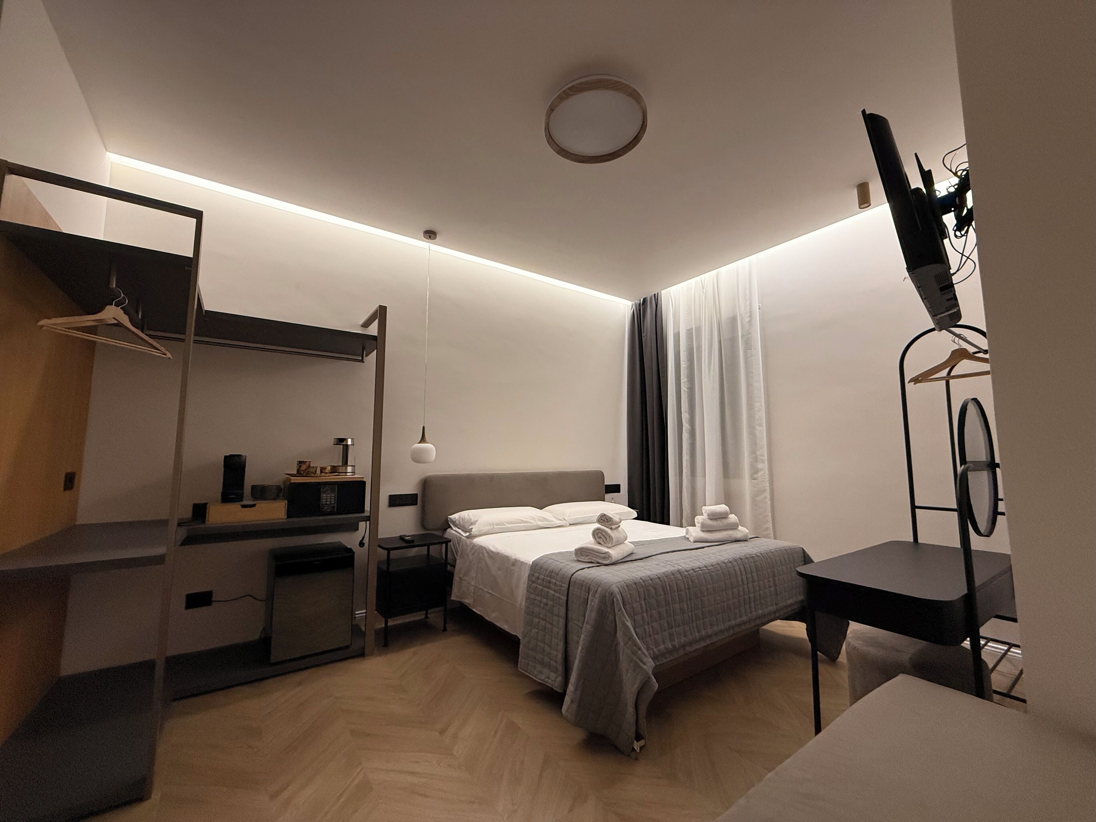 A modern hotel room with a bed, bedside table, and a desk with a chair.