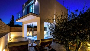 Ein modernes, zweistöckiges Haus mit Pool, Außenbereich zum Sitzen und einer gut beleuchteten Terrasse.