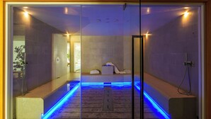 Ein modernes Spa mit Glastrennwand, warmer Fußboden und einem Entspannungsbereich mit Massagegerät und Handtüchern.