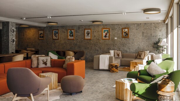 Un salon moderne avec un canapé, des fauteuils et une table basse. Des tableaux encadrés ornent le mur, et une plante est placée sur le côté.