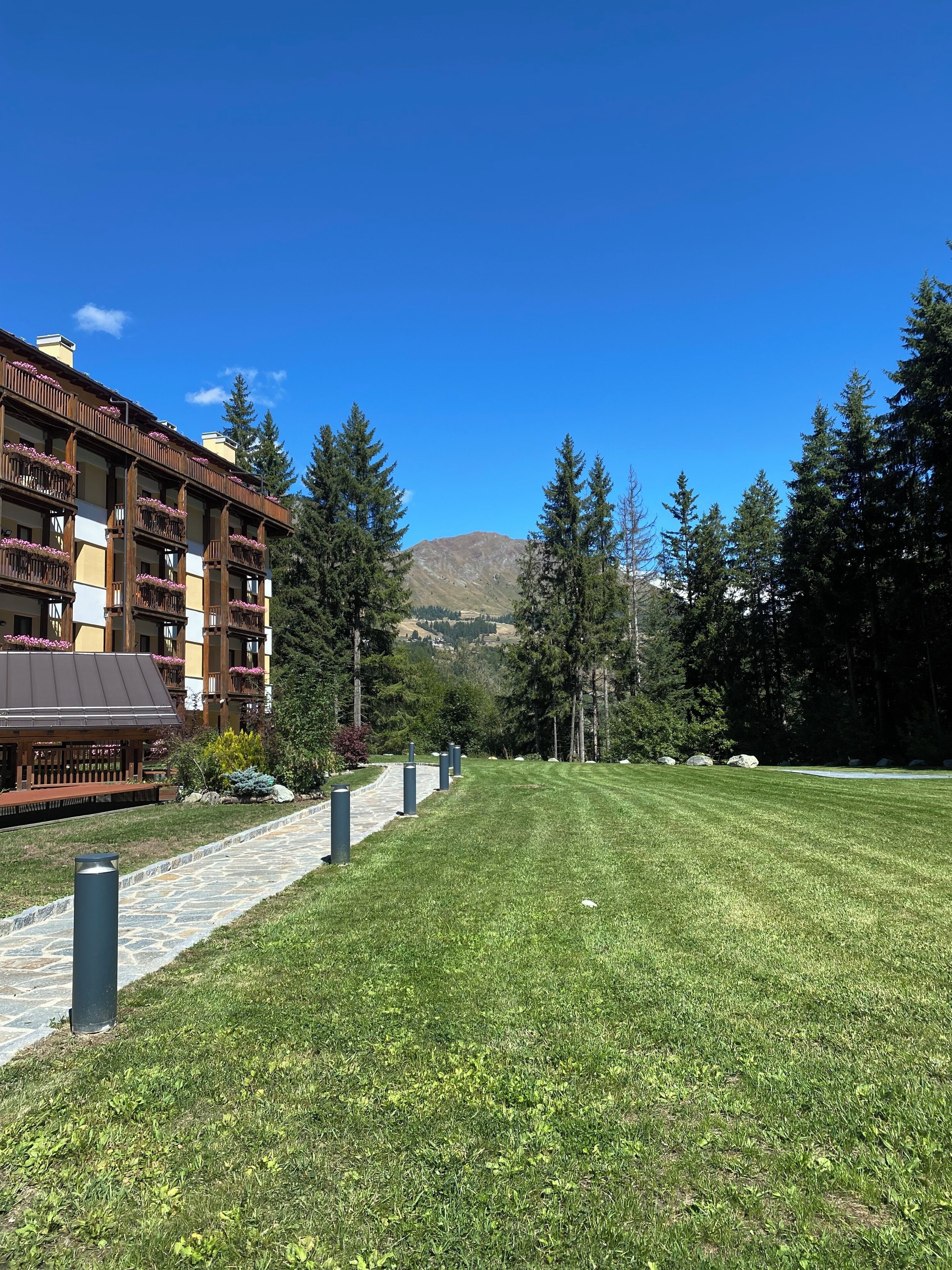 Un hôtel avec un chemin de pierre menant à une zone herbeuse, entourée d’arbres et avec une montagne en arrière-plan.