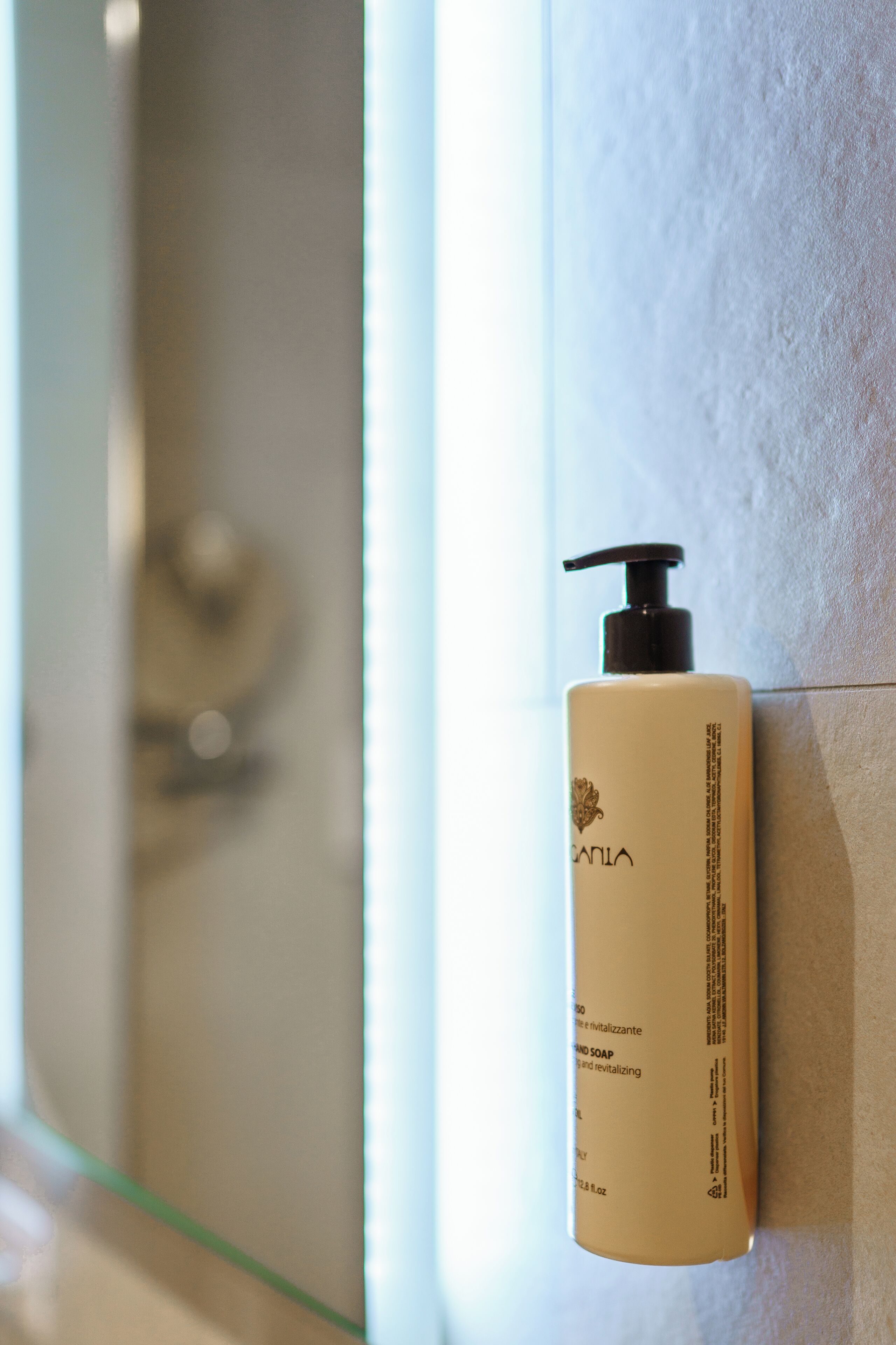Une salle de bain avec un flacon de savon liquide de couleur beige posé sur un mur carrelé.