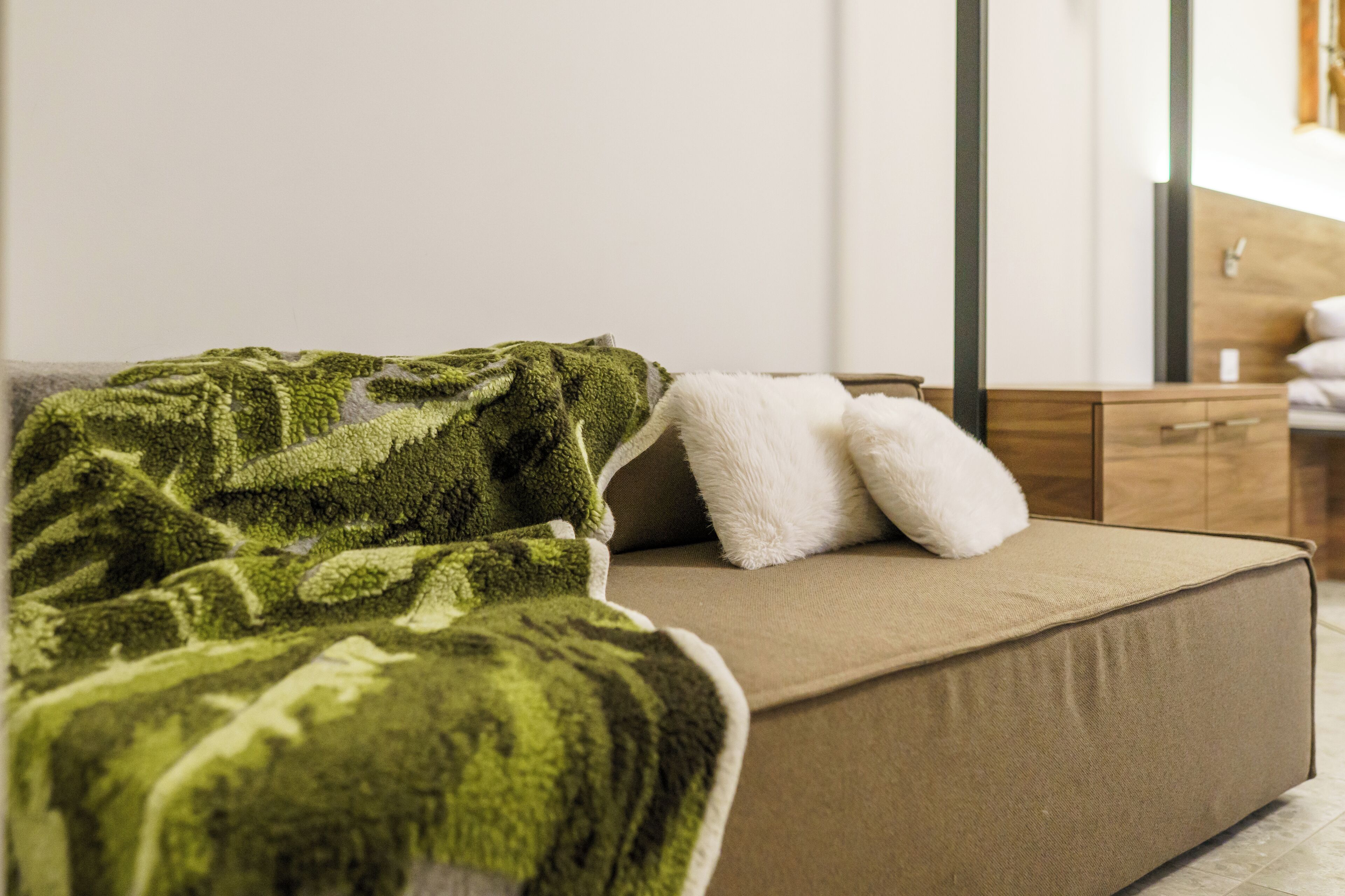 Ein Bett mit grüner Decke und weißen Kissen, ein Nachttisch aus Holz und ein Spiegel an der Wand.