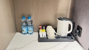 A hotel minibar with bottled water, coffee pods, a coffee maker, and a tea kettle. - Amaris Hotel (Barka)