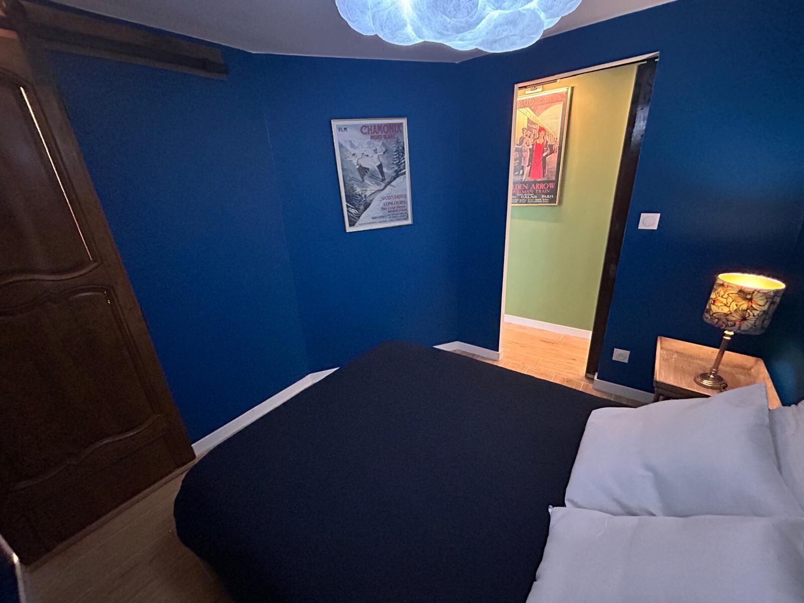 Een slaapkamer met een bed, een poster aan de muur, een lamp en een deur.