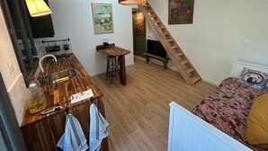 Un espace de vie compact comprenant un coin cuisine, une table à manger, un canapé, un escalier et un luminaire suspendu.
