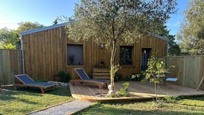 Une terrasse en bois avec deux chaises longues et une petite table, entourée d’une clôture en bois et d’un arbre.