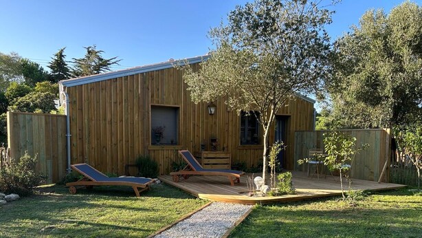 Une construction en bois dotée d’une terrasse, de deux chaises longues et d’un petit arbre.