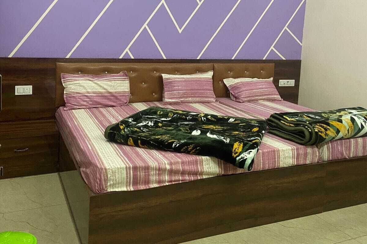 Une chambre à coucher avec un lit, une tête de lit, un mur orné d’un motif géométrique, un ventilateur de plafond et une poubelle verte.