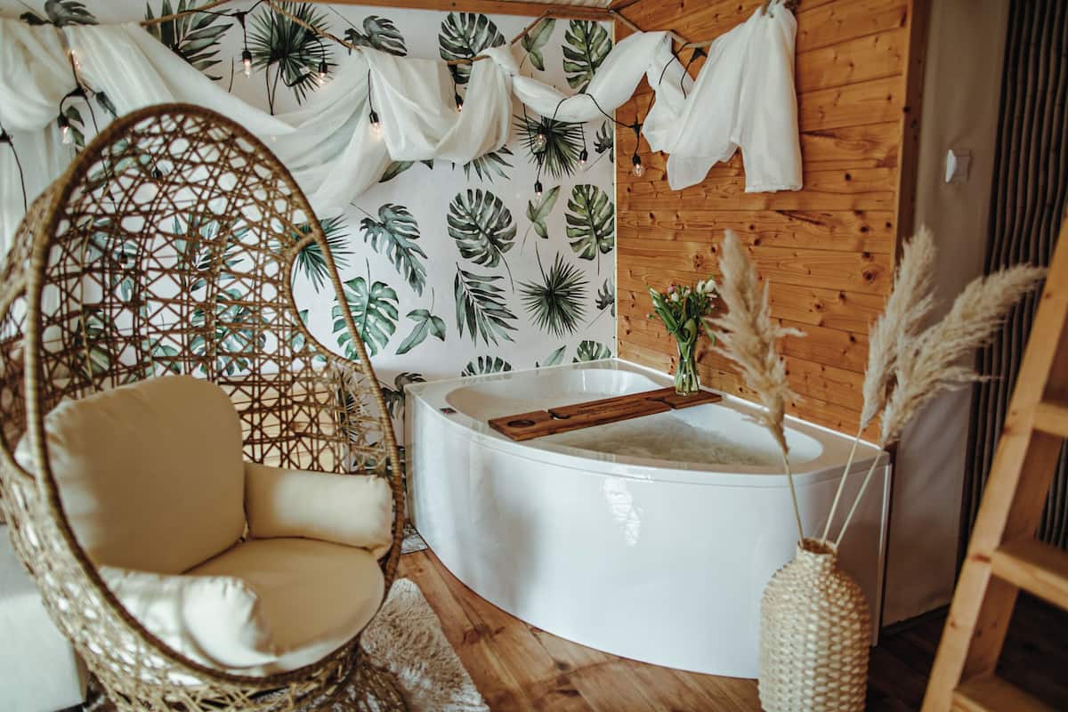 Um quarto acolhedor com uma cadeira de vime, uma banheira branca e uma parede decorada com motivos de folhas tropicais.