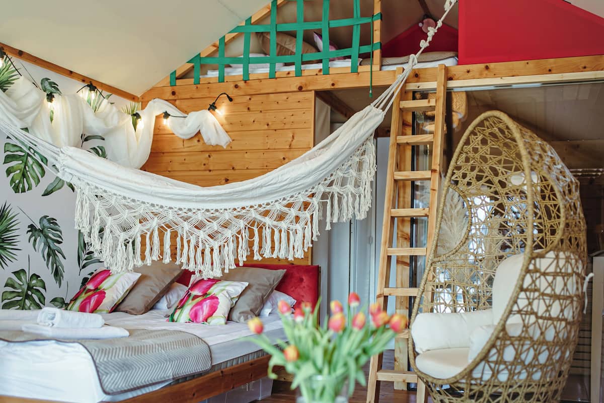 Um quarto aconchegante com uma rede, uma cadeira suspensa e uma cama com almofadas florais.