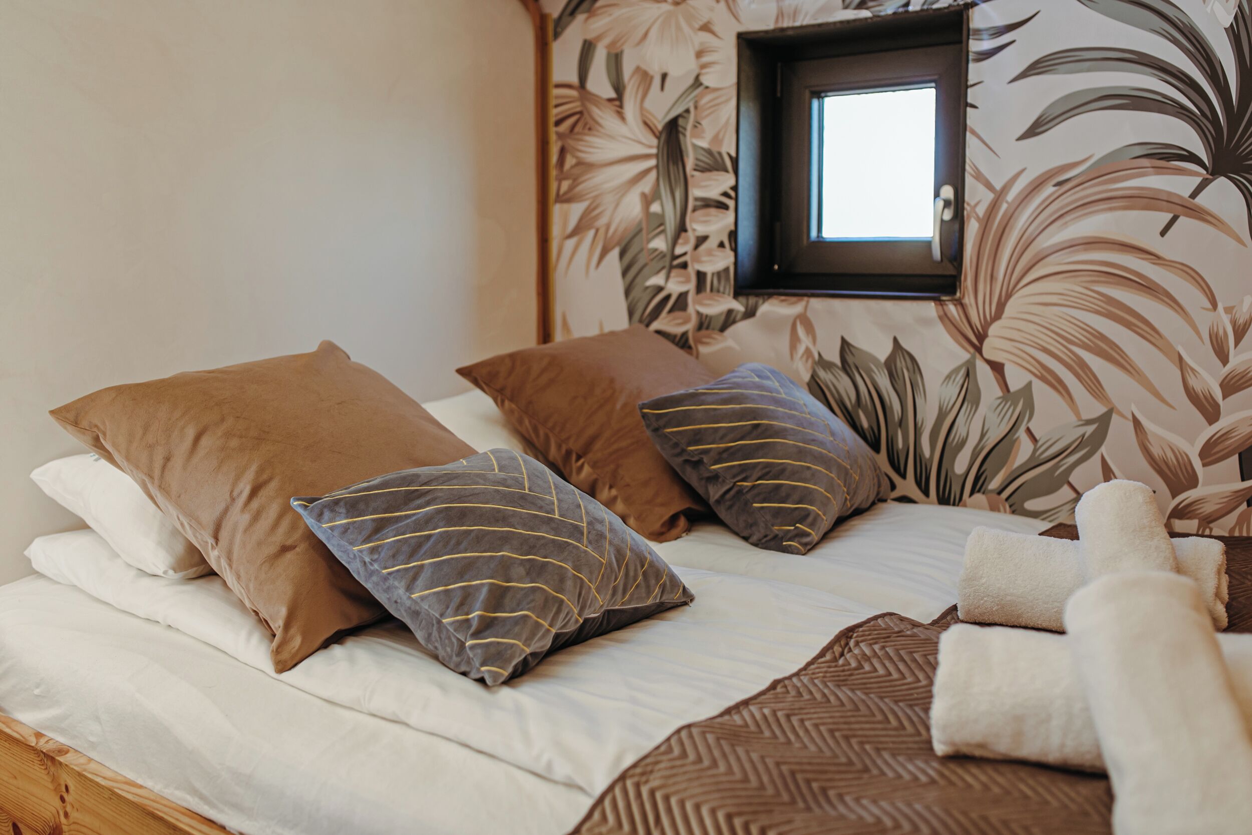 Un letto con numerosi cuscini e una coperta, una finestra e un motivo floreale sulle pareti.