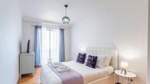 Et pænt opredt soveværelse med seng, sengebord, lampe og udsigt til det fri.