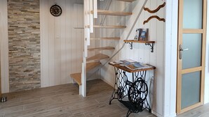 Eine Holztreppe mit einer weißen Wand und einer Wandverkleidung aus Stein. Ein kleiner Tisch mit Zeitschriften und ein Metallständer mit Namensschild.