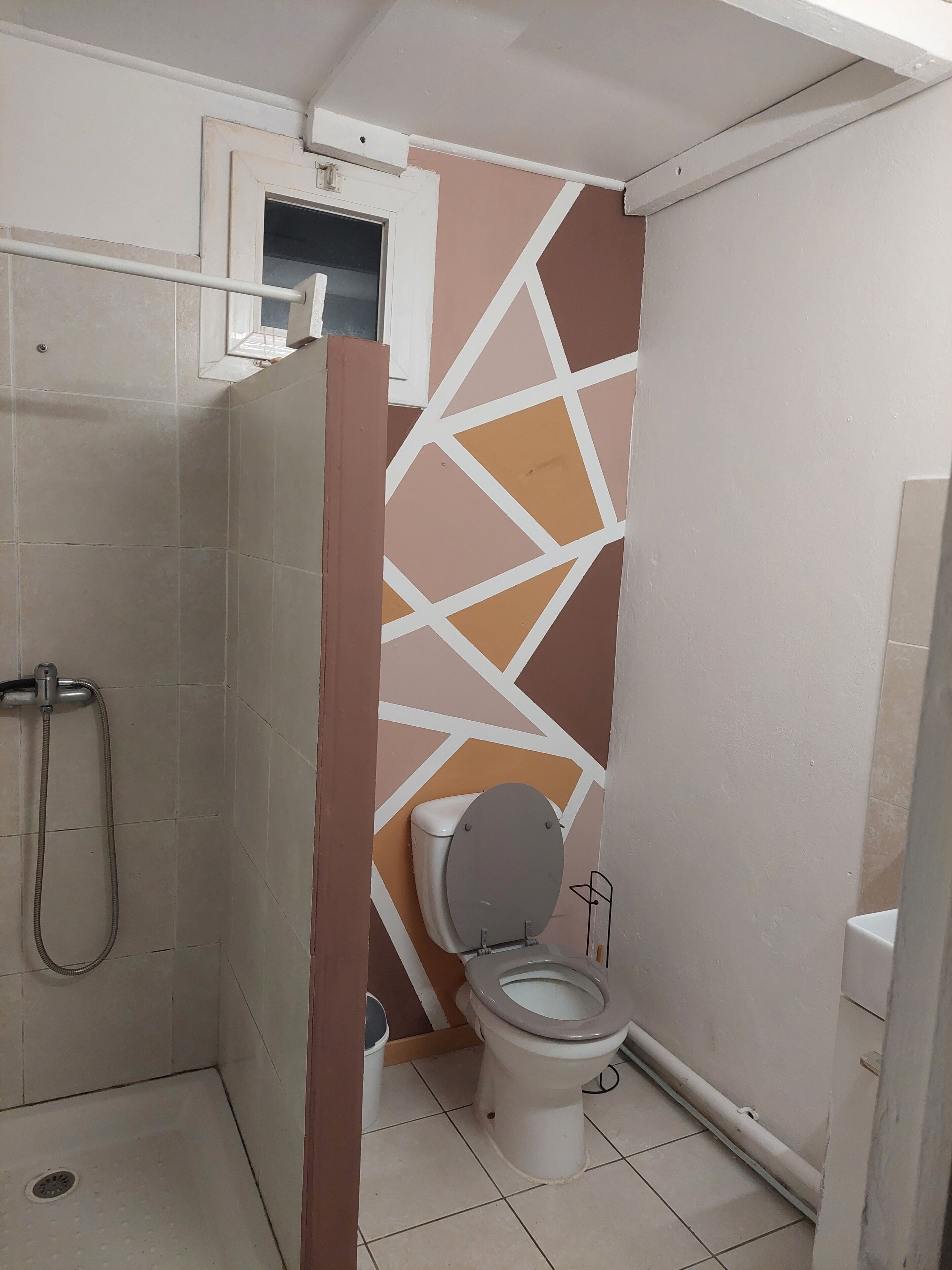 Kylpyhuone, jossa on suihku, wc ja seinä, jossa on geometrinen kuvio.