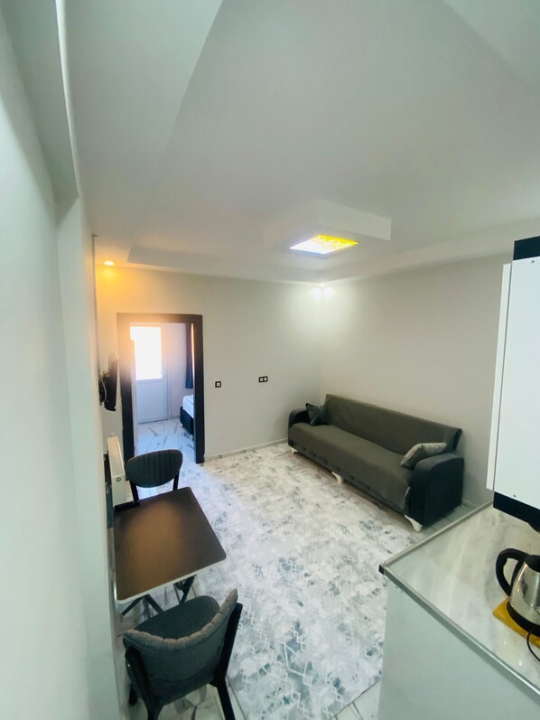 Una sala de estar con un sofá, una mesa y una silla. Se ve una puerta que da a otra habitación.