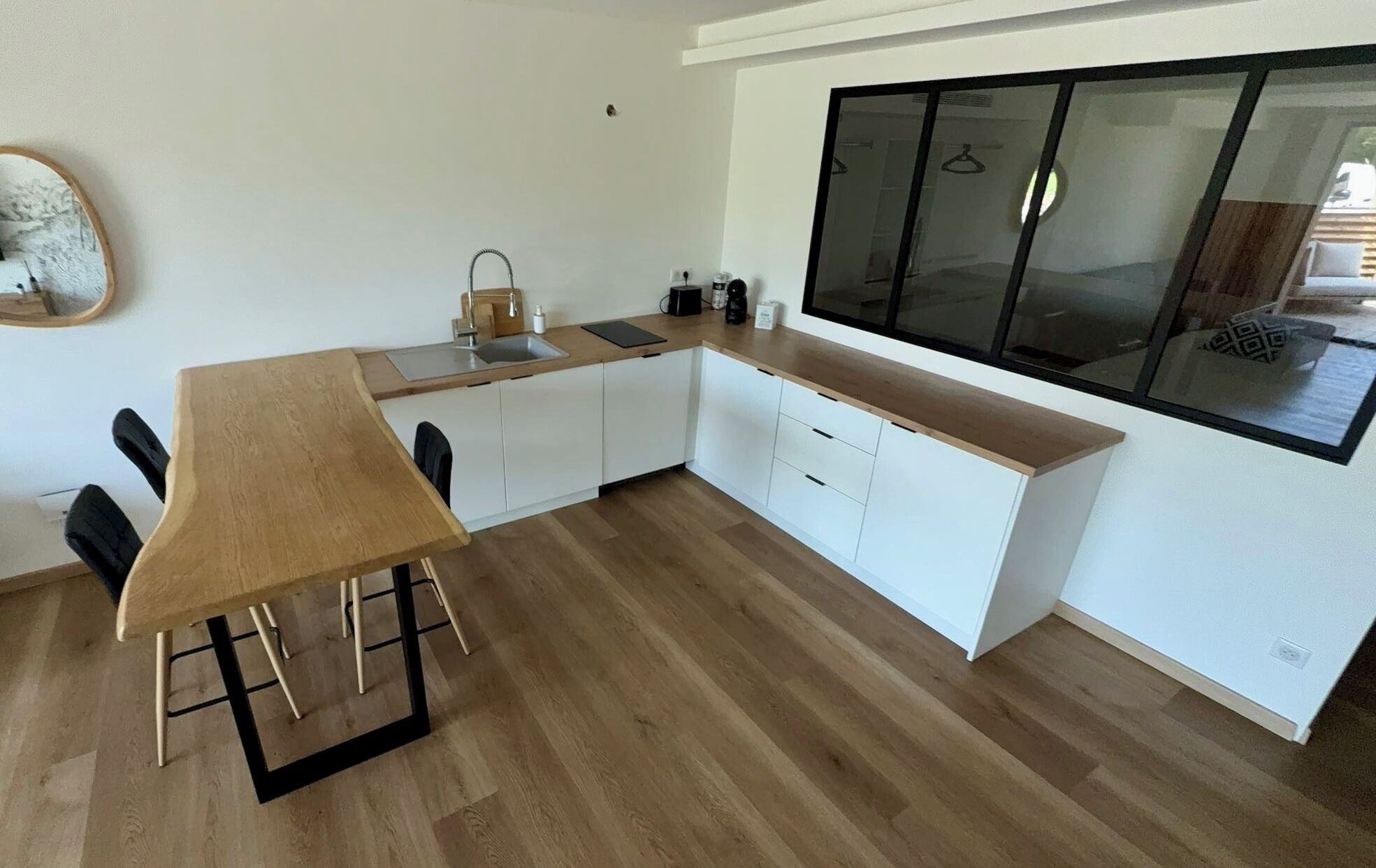 Una cocina moderna con mesa y sillas de madera, armarios blancos y un ventanal grande.