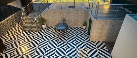 A rooftop terrace with a geometric patterned floor, a small seating area, and a pool with a textured wall.