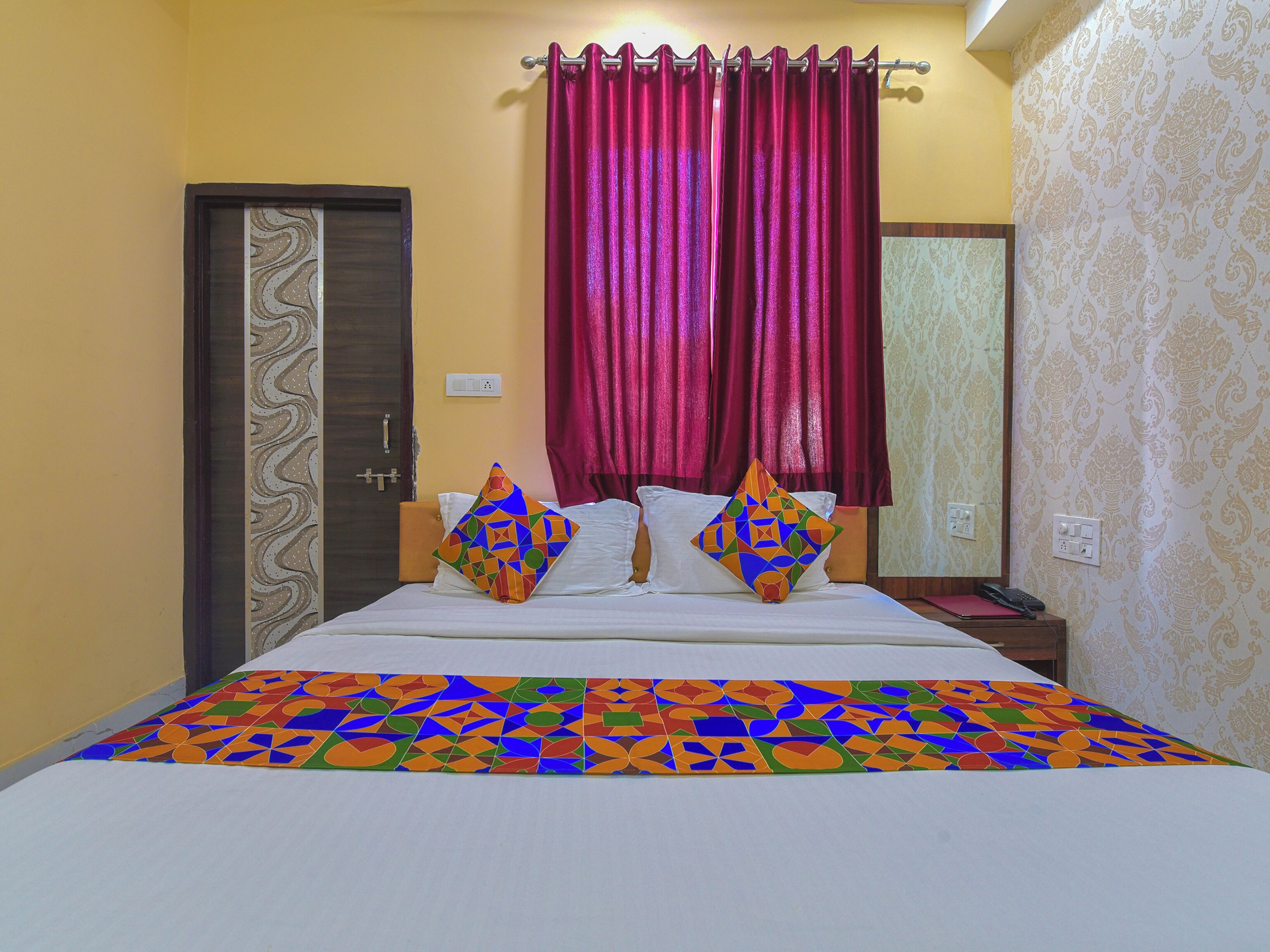 A bed with colorful geometric pillows, a red curtain, and a patterned wall.