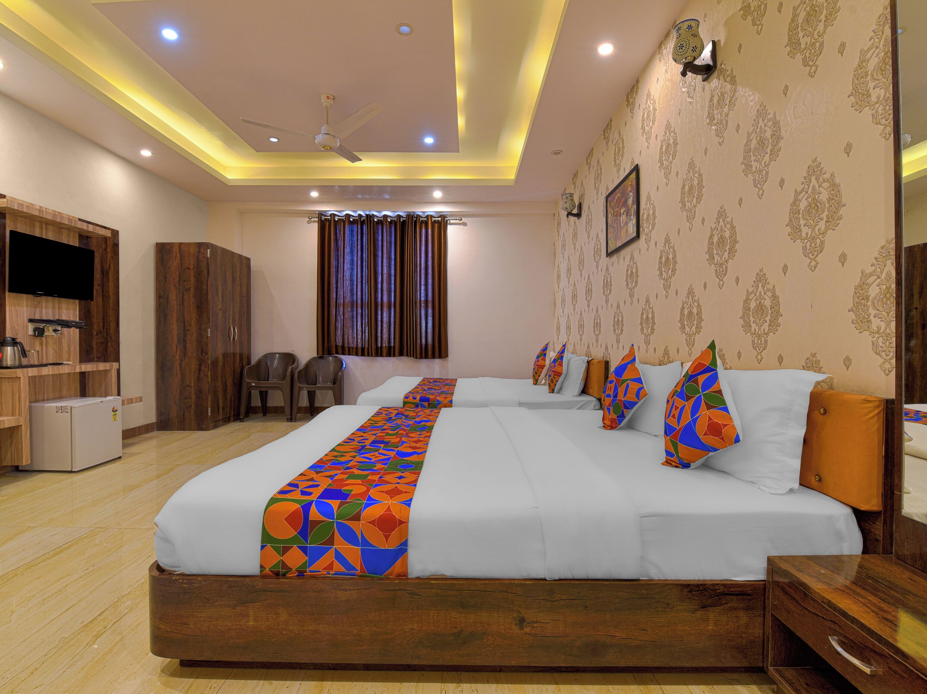A hotel room with a large bed, a TV, a wardrobe, and a desk with a lamp.