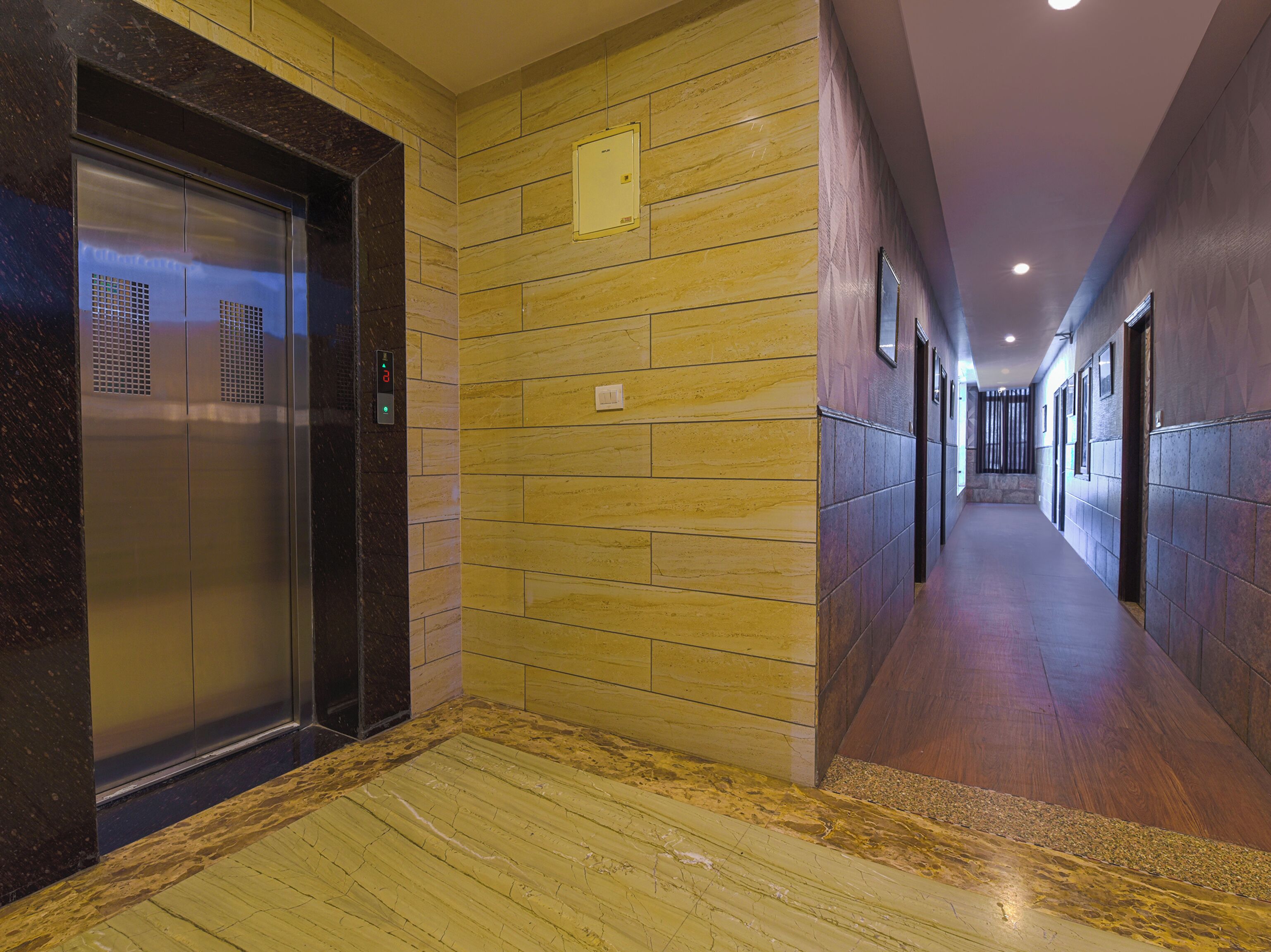 A modern hallway with a marble floor, a wall-mounted elevator, and a long corridor with doors on one side.