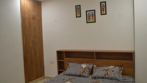 A bedroom with a wooden wardrobe, a bed with floral bedding, and three framed pictures on the wall.