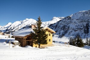 A wooden cabin with a snow-covered roof, surrounded by a snowy landscape and mountains. - House Obdr Lech (Lech)