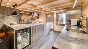 Una cocina moderna con vigas de madera en el techo, una isla central, electrodomésticos de acero inoxidable y un refrigerador con puerta de vidrio.
