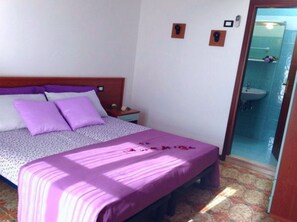 A bedroom with a bed, nightstand, and a bathroom visible through an open door. - Elegant Apartment Near the Beach (San Michele al Tagliamento)