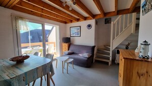 Una habitación acogedora con techo de madera, un sofá, una mesa con sillas y una escalera.