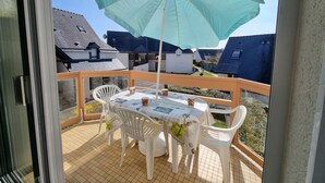 Un balcón con una mesa, sillas y un paraguas grande, con vista a casas vecinas.