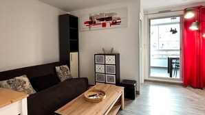 A modern living room with a sofa, a wooden coffee table, a black cabinet with geometric patterns, and a red curtain. - Air-conditioned apartment with parking and wifi 150m from the beach (Canet-en-Roussillon)