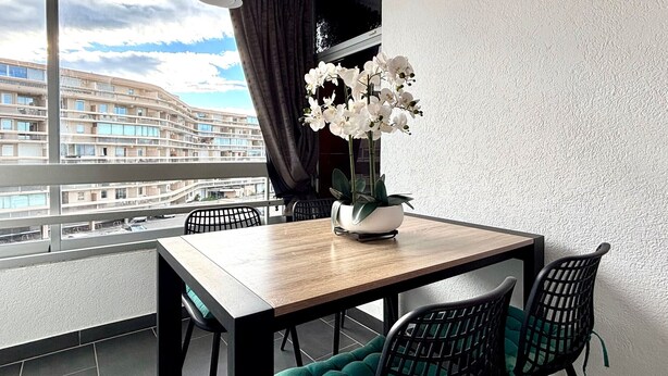 A modern dining area with a wooden table, black chairs, and a potted orchid. - Air-conditioned apartment with parking and wifi 150m from the beach (Canet-en-Roussillon)