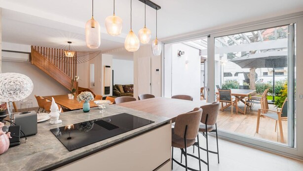 A modern kitchen with a central island, pendant lighting, and a view to an outdoor patio area. - Villa in Central Le Touquet with Air Conditioning and Wifi (Le Touquet-Paris-Plage)