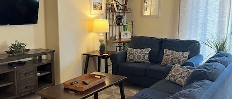 A living room with a dark blue sofa, a coffee table, a TV, and a ceiling fan.