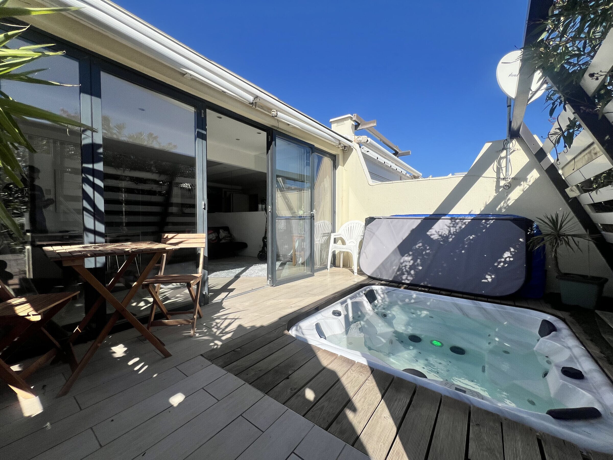 Eine Terrassenanlage mit Whirlpool, Holzterrasse und Glastür zu einem Zimmer.