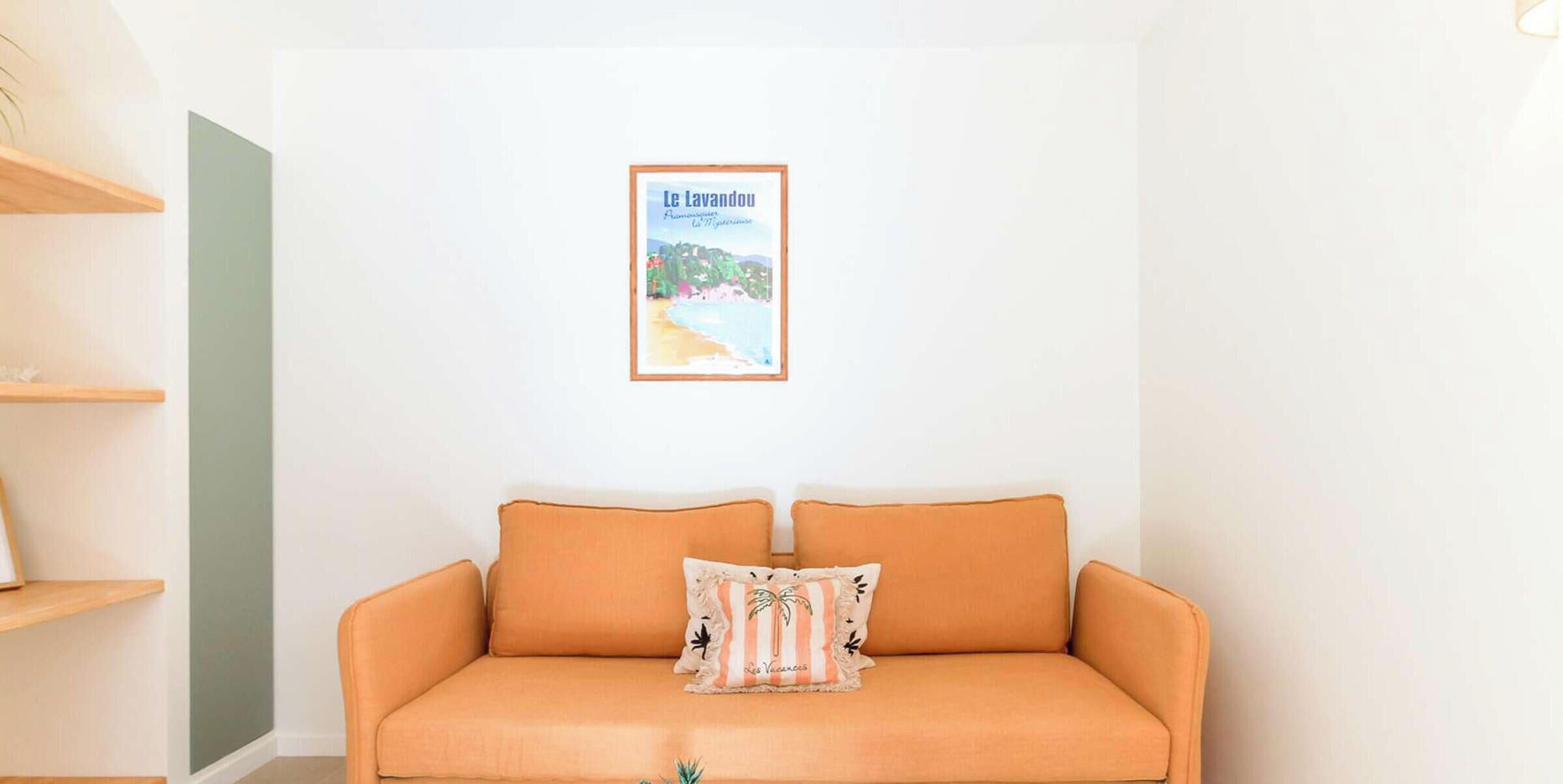 A room with a single orange sofa, a framed picture on the wall, and wooden shelves.
