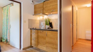 Cocina compacta con armarios de madera, cafetera y planta en la encimera.