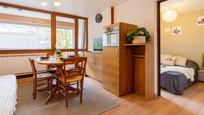 Cocina compacta con gabinetes de madera, una mesa de comedor con sillas, horno empotrado y ventana que proporciona luz natural.