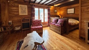 Een knus houten blokhutkamer met een bed, een stoel, een houten bijzettafeltje en een open haard.