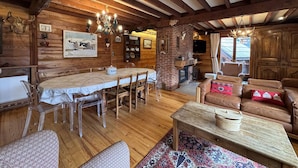 Een landelijk chalet interieur met een eethoek, open haard, leren bank en houten balken.