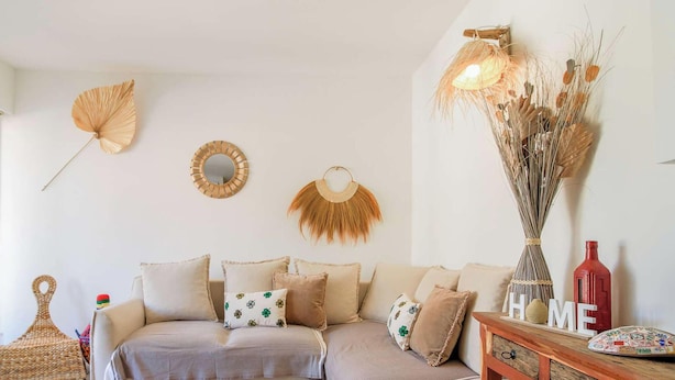 Ein Wohnzimmer mit einem beigefarbenen Sofa, dekorativen Wandspiegeln und einer Vase mit Trockenpflanzen.