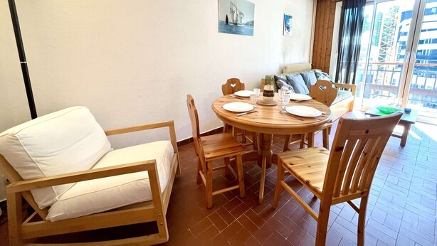 A cozy room with a round wooden dining table set for four, a white sofa, and a bed with a wooden frame. - Mountain Studio in Claux, 4 people, close to slopes & shops (Vars)