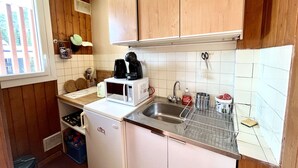 A compact kitchen with wooden cabinets, a white refrigerator, a microwave, a sink with a stainless steel basin, and a window with blinds. - Mountain Studio in Claux, 4 people, close to slopes & shops (Vars)