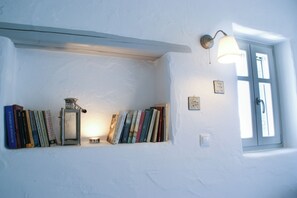 A bookshelf with books and a metal lantern, a wall-mounted light fixture, and a window with a door. - House with private pool (Kamares Naousas)