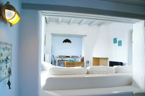 Ein weißes Sofa in einem Raum mit Holzbalkendecke, einem Tisch mit Stühlen und einer Wanduhr.