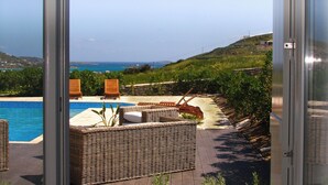 An open door to a patio with a pool, wicker furniture, and a view of the coastline. - House with private pool (Kamares Naousas)