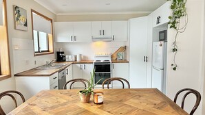 A modern kitchen with white cabinets, a wooden dining table, and a hanging plant.